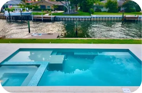 Pool and raised square spa with a canal and boat dock visible behind the yard.