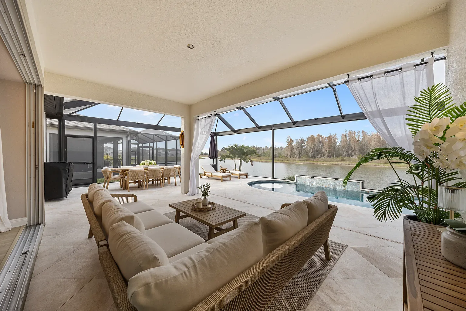 Covered lanai with sectional seating and an outdoor dining set, opening onto a screened pool deck and lake in Wesley Chapel, Florida.