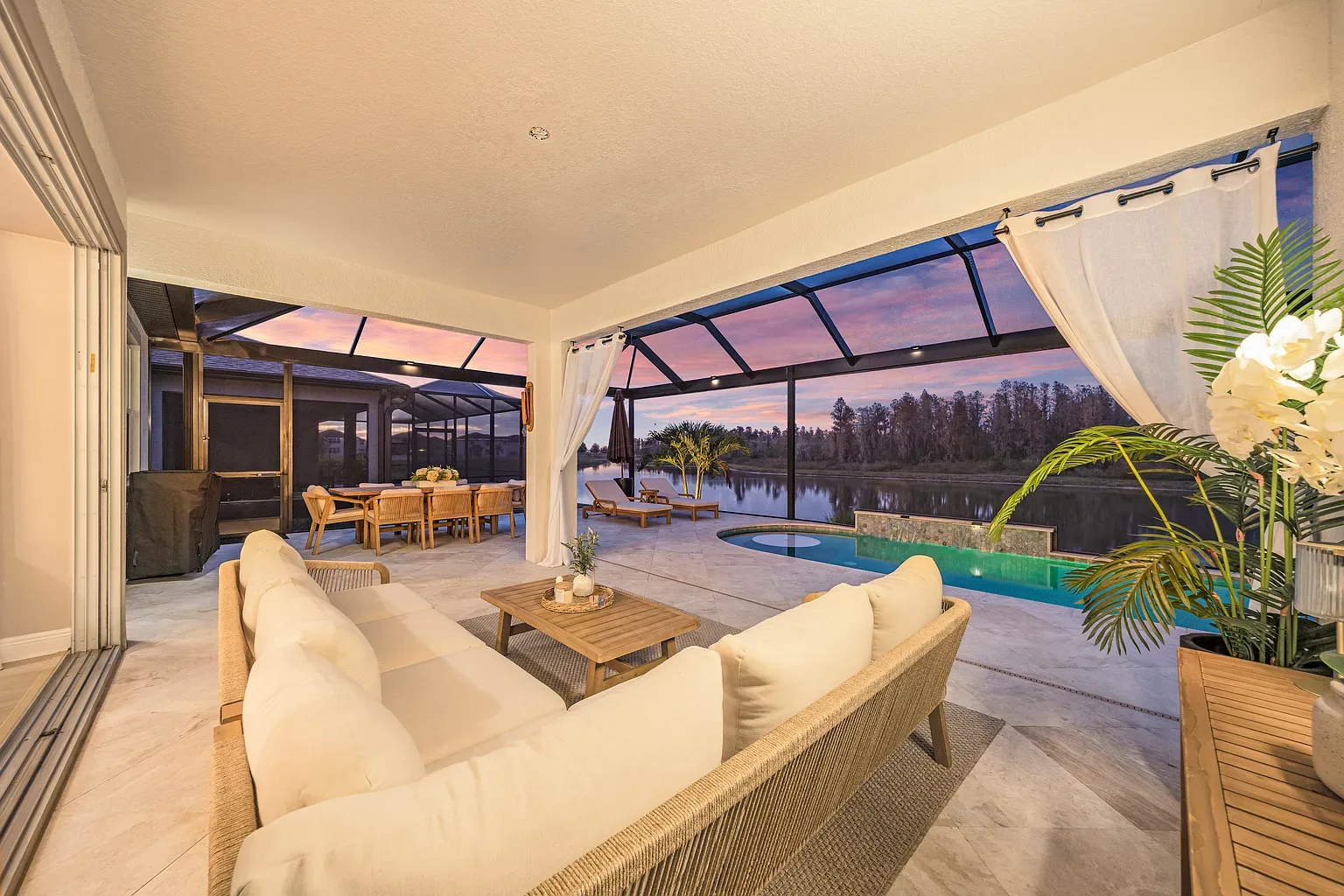 Covered lanai and screened pool deck at dusk, lit against a pink sunset over the lake, Wesley Chapel, Florida.