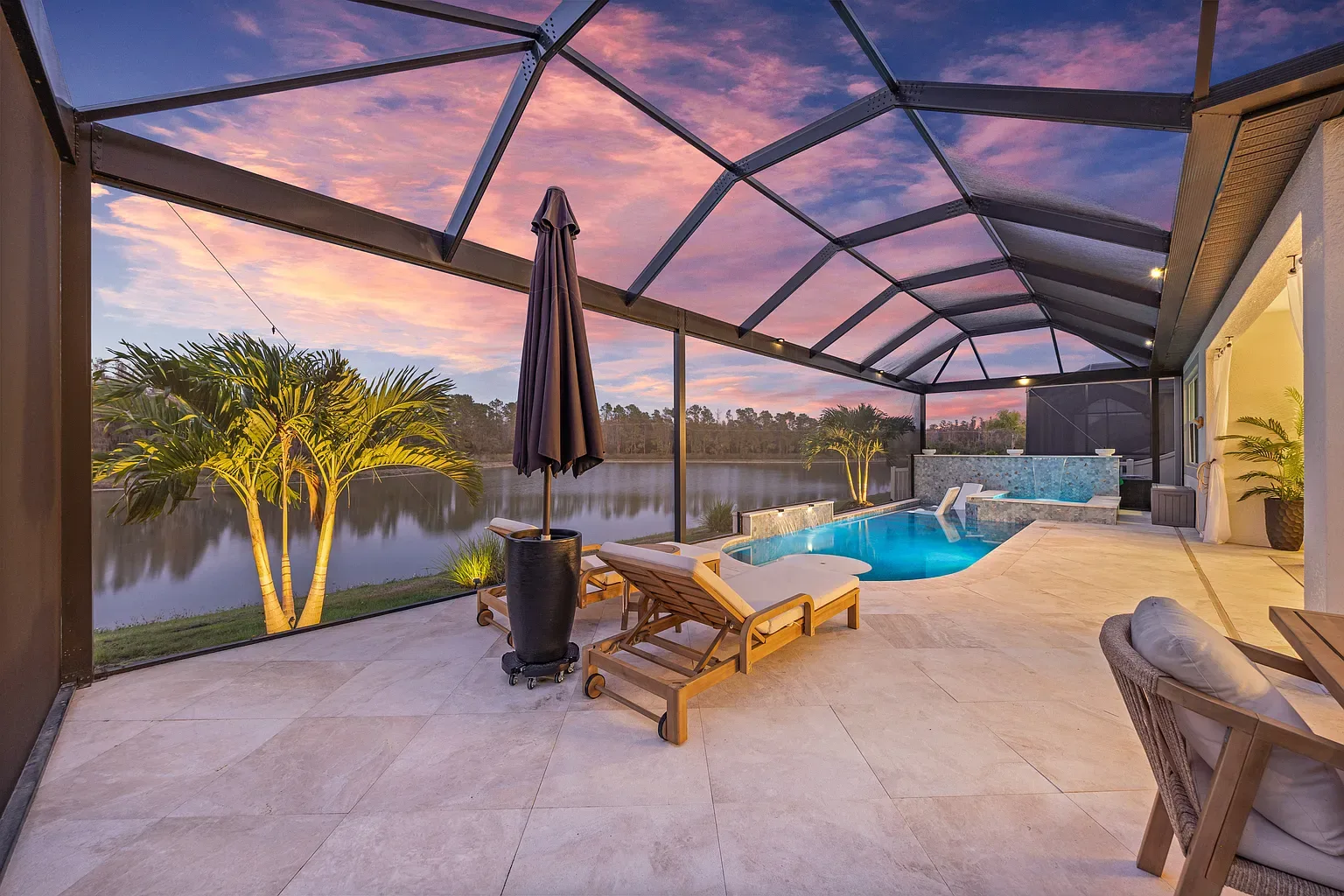 Screened pool deck at dusk with uplit palms and a pink sky over the lake, Wesley Chapel, Florida.
