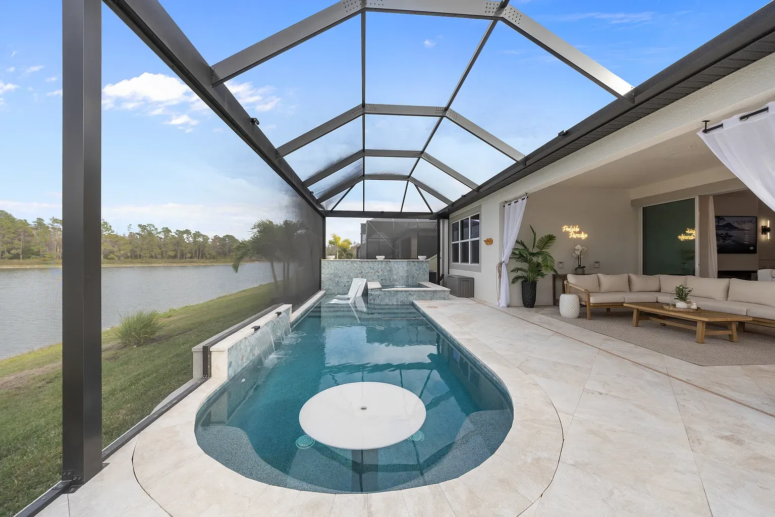 Full length of a linear pool with an in-pool umbrella table, sun shelf and raised spa, lake beyond the screen enclosure, Wesley Chapel, Florida.