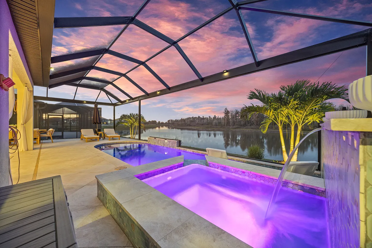 Raised spa lit purple at dusk, its waterfall running into the pool beneath a sunset sky, Wesley Chapel, Florida.