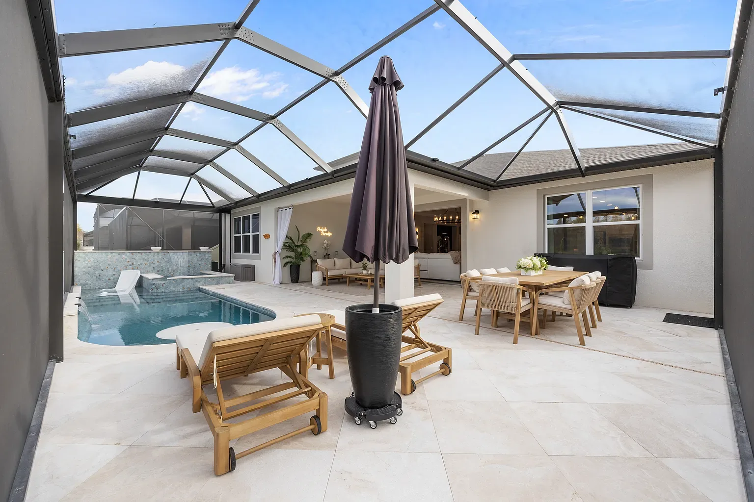 Travertine pool deck with teak loungers and an outdoor dining set under a screen enclosure, Wesley Chapel, Florida.