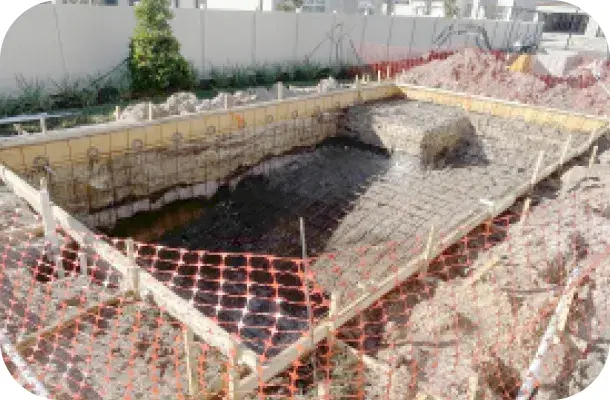 Pool shell mid-construction with rebar and wooden forming stakes in place, no water yet.
