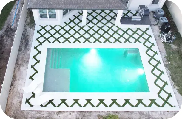 Aerial dusk view of the finished pool with turquoise water and diamond-pattern sod.