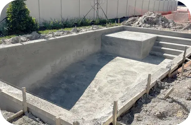 Pool shell mid-construction with poured concrete steps and grading stakes.